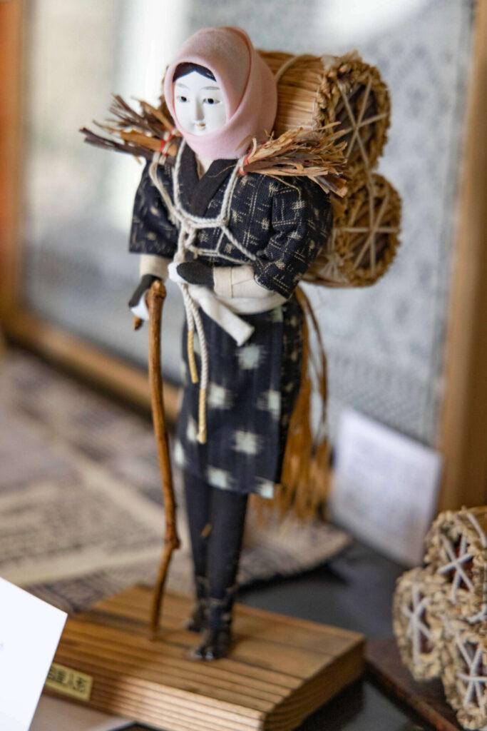 西目屋村の県伝統工芸品「目屋人形」。炭俵を背負い、杖を突いて山道を行く女性を象っています。