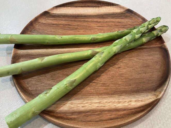軽く洗われたアスパラガスが皿に並べられ、みずみずしさが伝わる春の緑野菜。